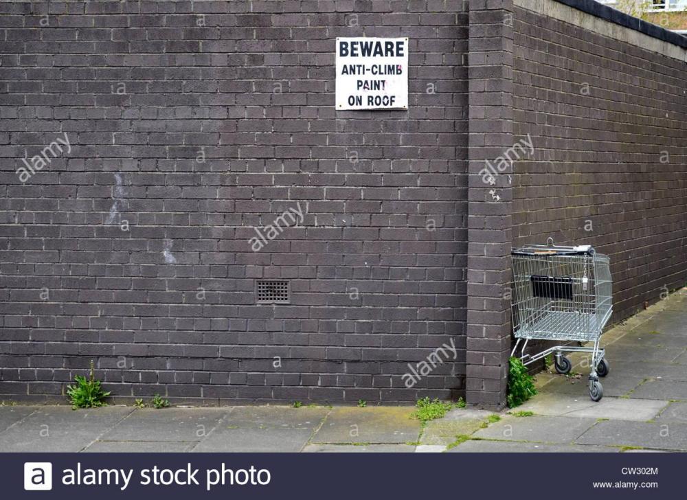 an-abandoned-supermarket-trolley-and-a-wall-with-a-sign-warning-of-CW302M.jpg
